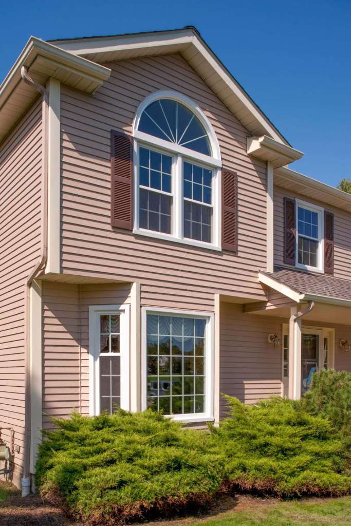 Two-story home with tan siding, double-hung windows and an arched accent window