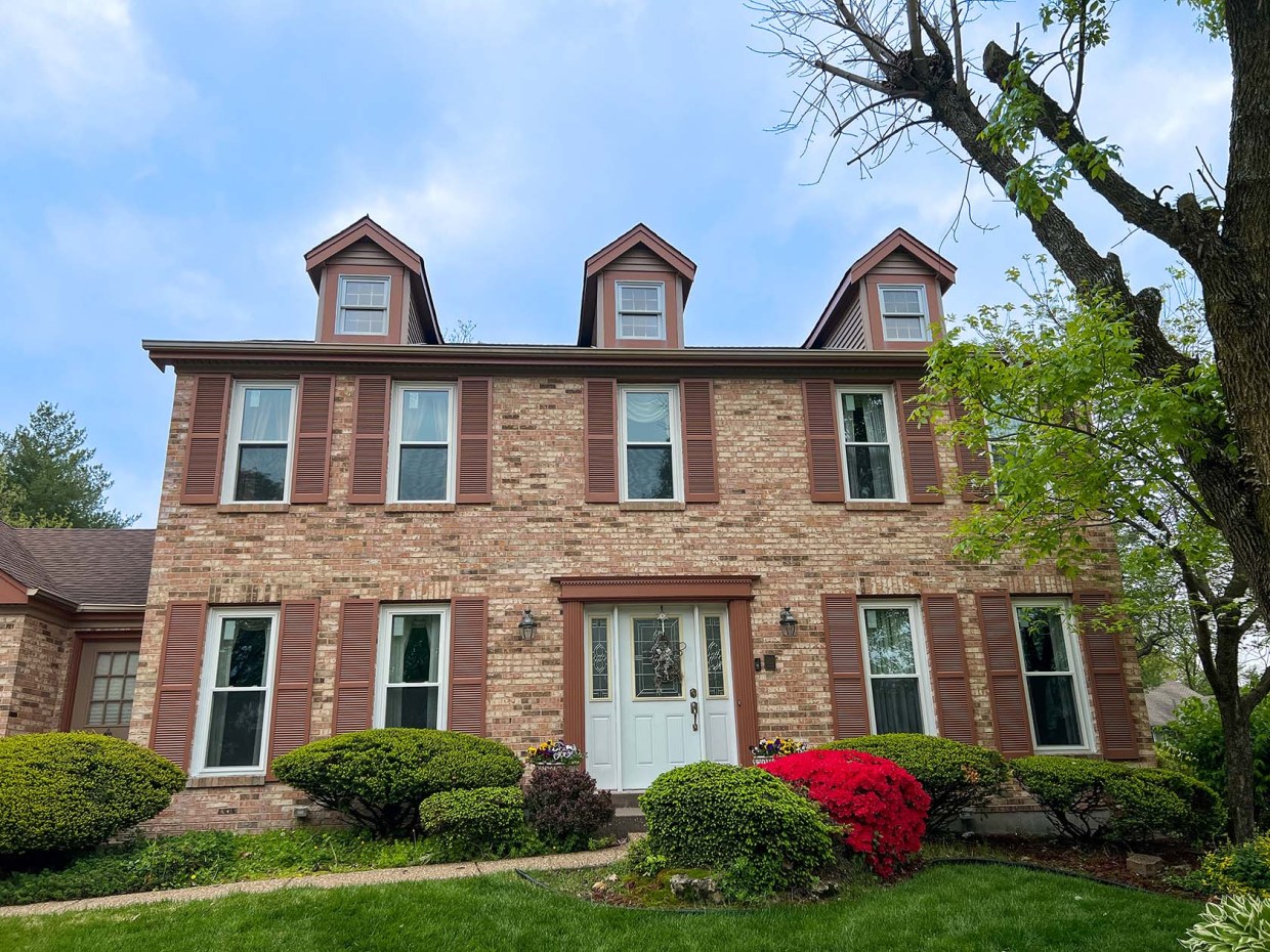 A brick house with brow shutters and multiple dormers.