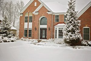 A brick home and surrounding landscape covered in snow.