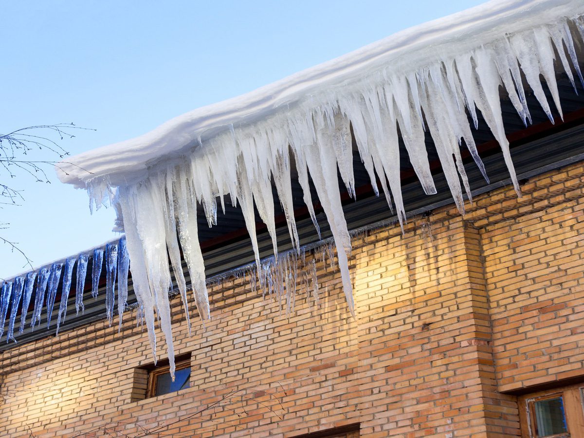 An ice dam and thick icicles hang from the side of a house.