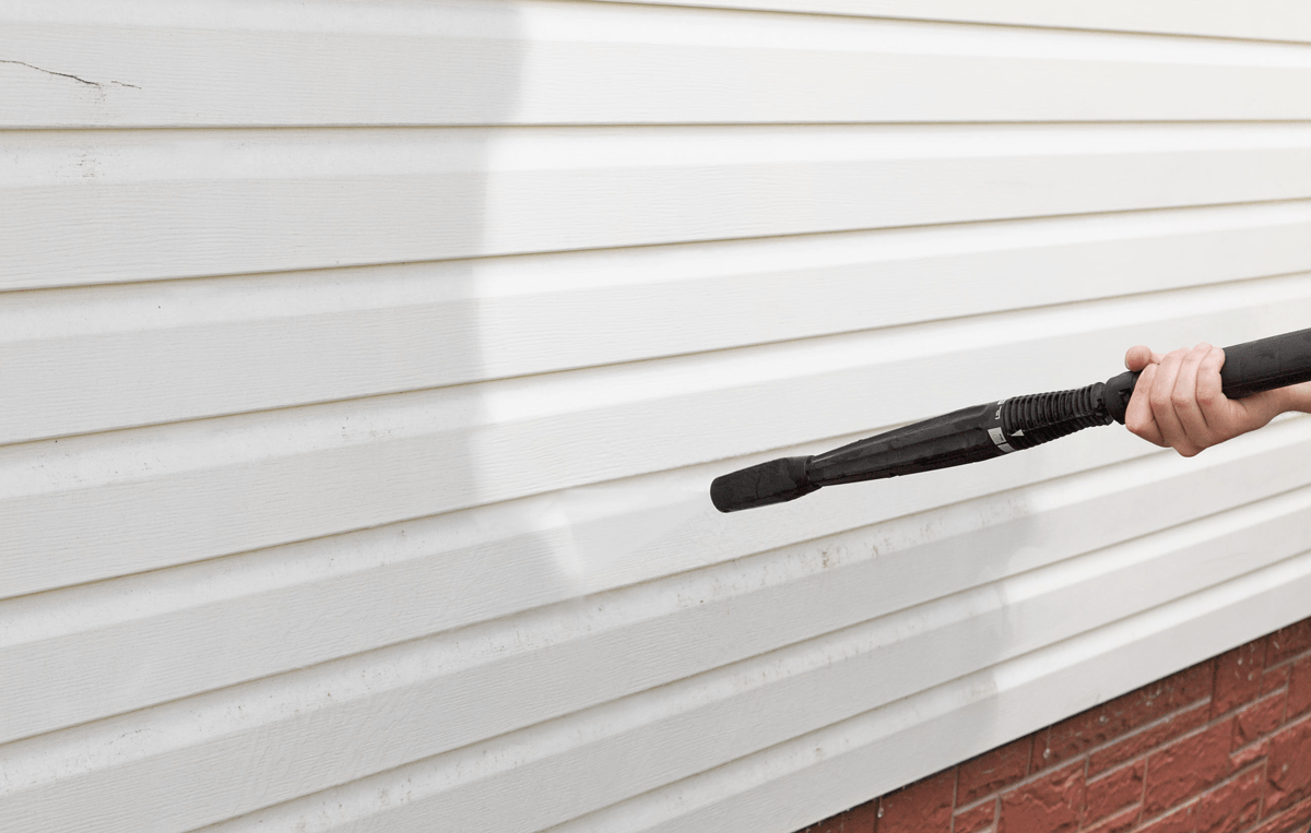 A power washer directed at the siding of a house.