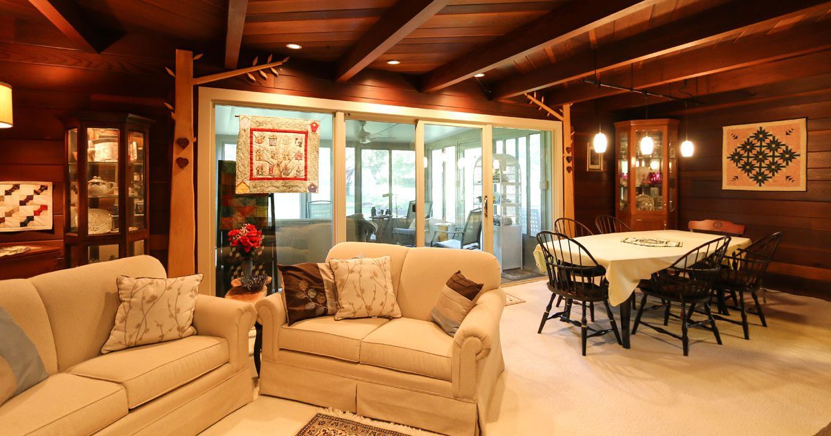A wood wall and ceiling living room with patio doors leading to a sunroom.
