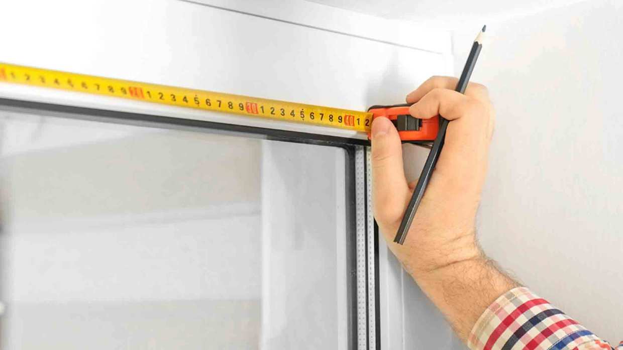 A measuring tap is held up to the corner of window glass.
