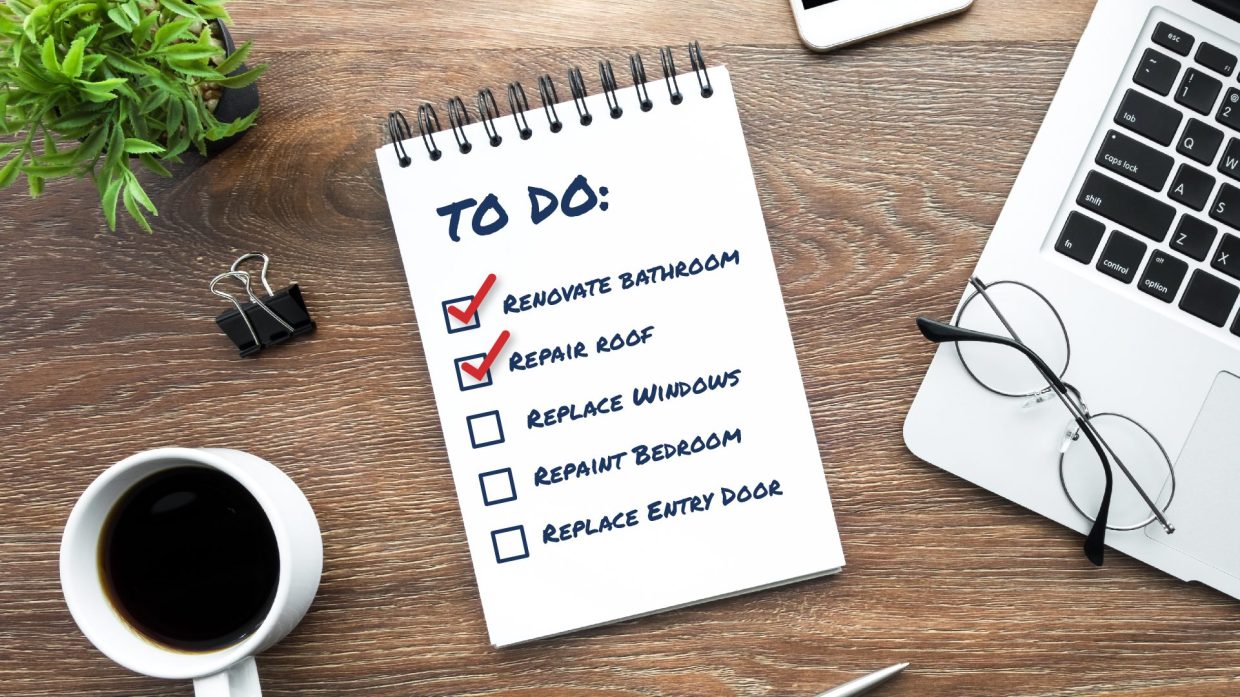 A desk with items on it including a to-do list that includes renovating a bathroom, repair roof, replace windows, repaint bathroom, replace entry door.