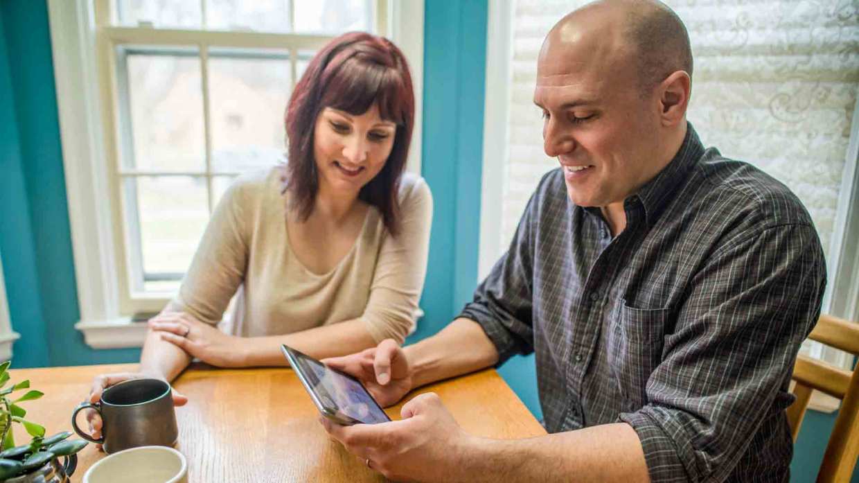 A man and a woman sit a dining table looking at a tablet.