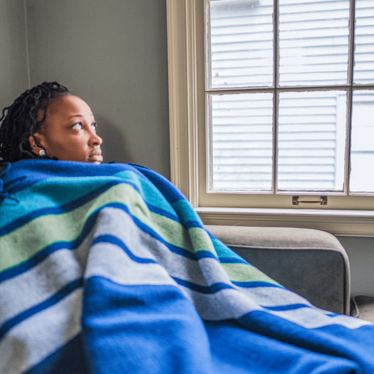 A woman covers herself in a blanked while looking concerned about her windows.