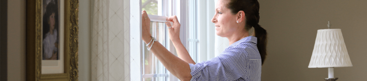 A woman lowers the window in her home.