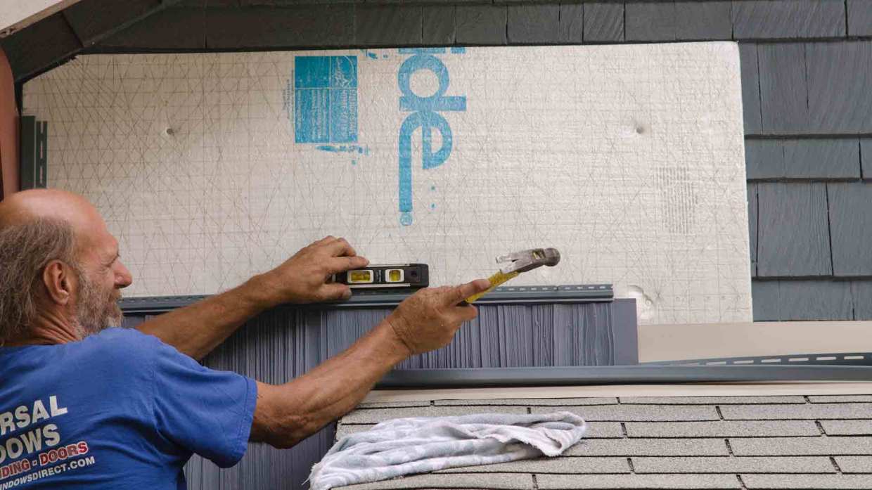 A Universal Windows Direct installer puts a piece of siding into place.