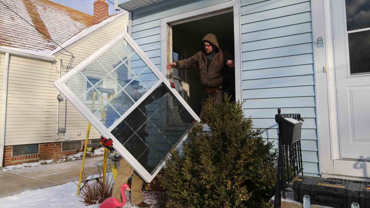 A pair of Universal Windows Direct pros lift a window to install it into a home.