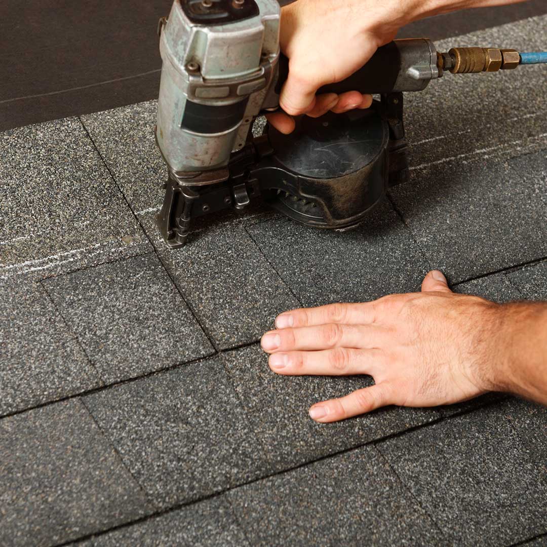 Roof Installation man installing shingles on roof with nail gun