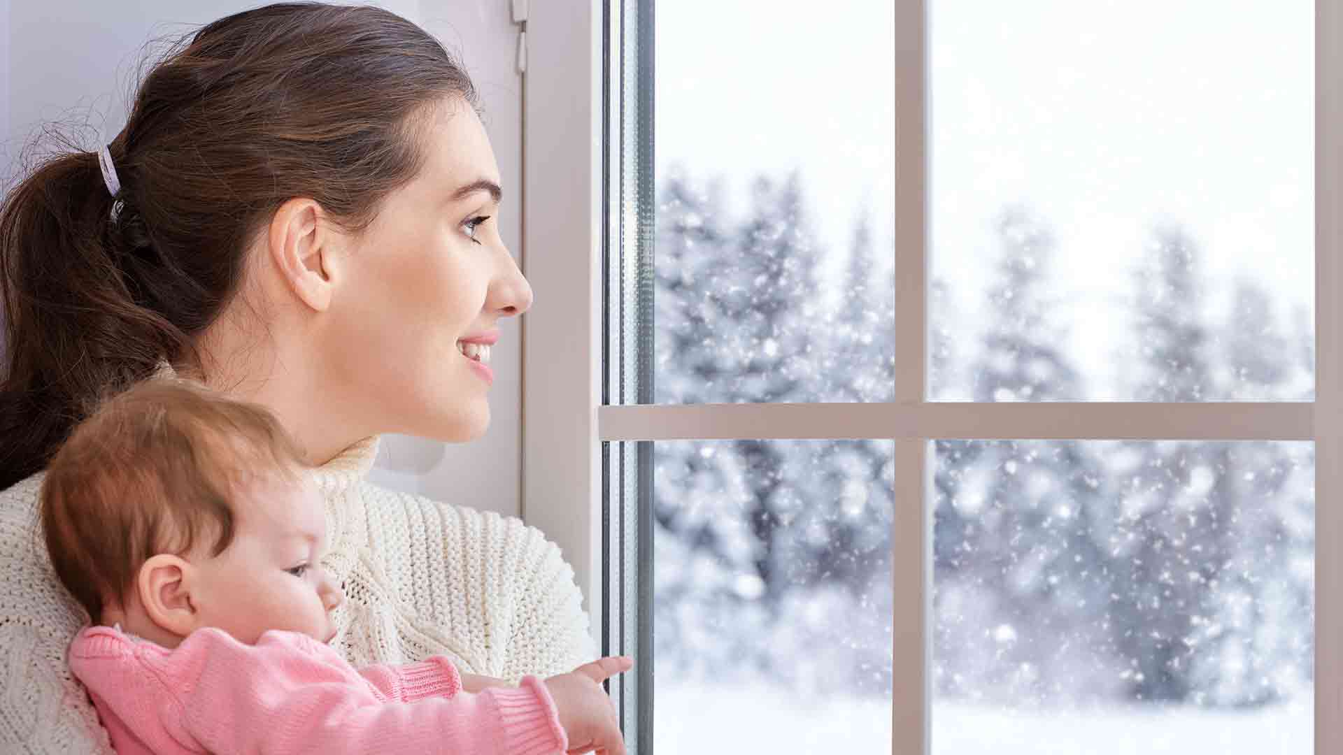 Mother holding baby, looking out window.