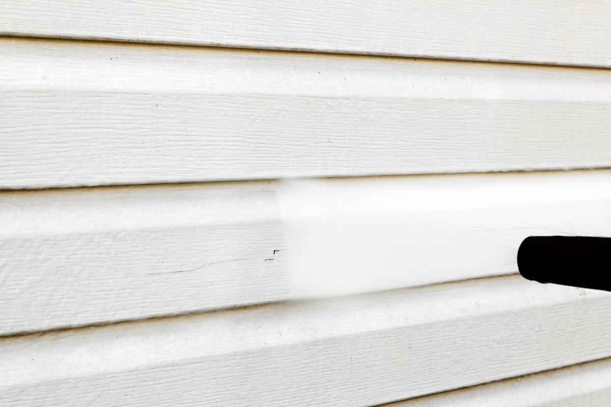 Close up of a power washer cleaning house siding.