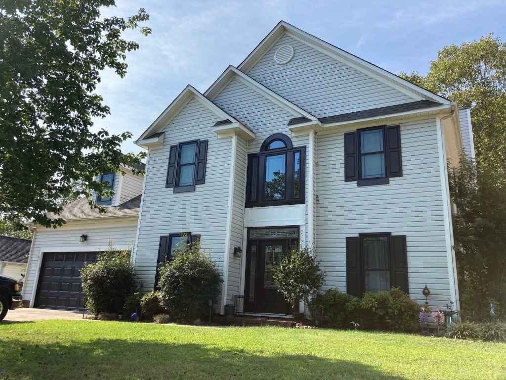 Curb-side view of a white house with black windows and shutters installed by Universal Windows Direct.