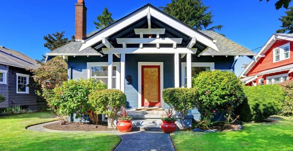 An exterior shot of the front of a blue house with white trim and a red front door.