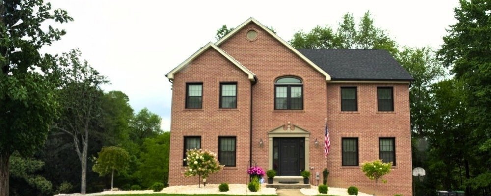 A 2-story brick home with black window frames surrounded by trees.