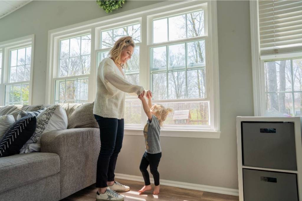 A mom dances with her daughter in front of newly installed windows in their living room.