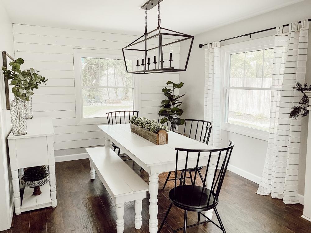A white, modern, country dining room with black fixtures and chairs is lit by windows installed by Universal Windows Direct.
