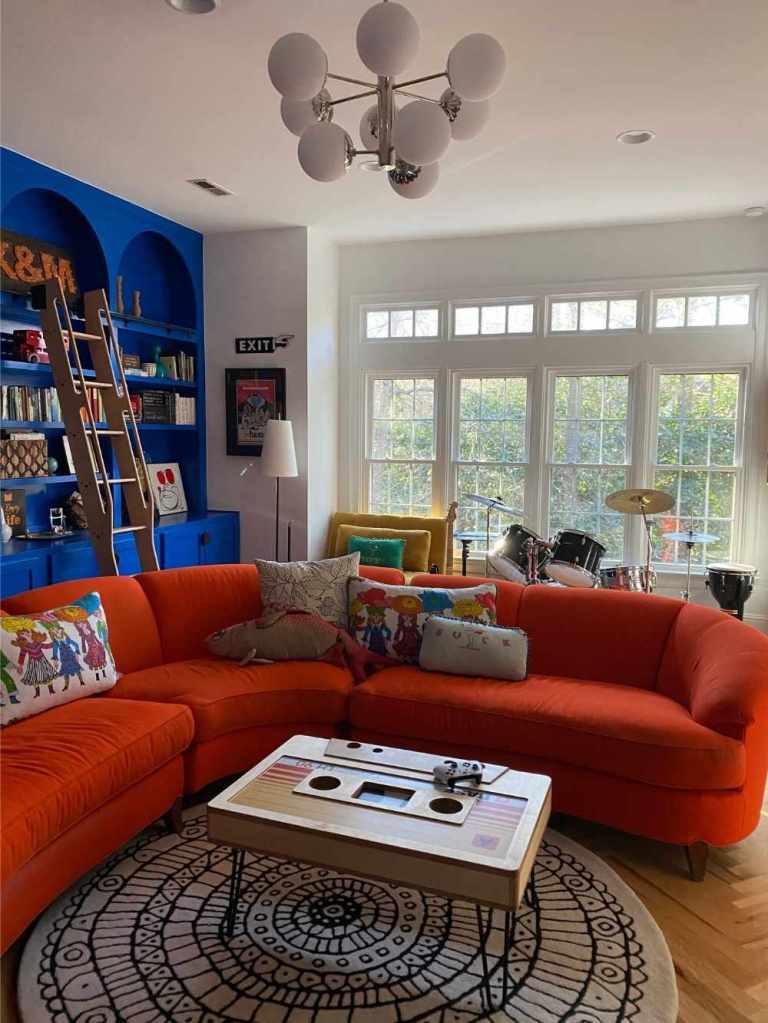 White gridded double hung windows installed by Universal Windows Direct illuminate a unique living room with a curving orange couch and cobalt blue built-in bookcases.