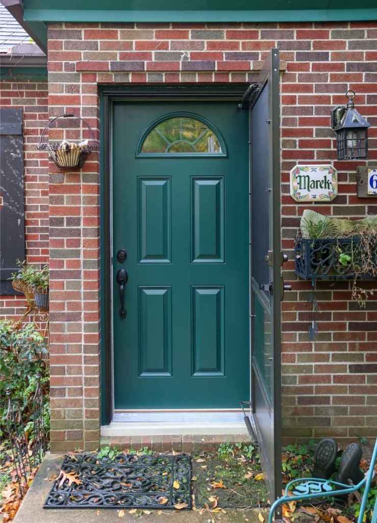 A green entry door with a half-moon glass window and an open storm door installed by Universal Windows Direct.