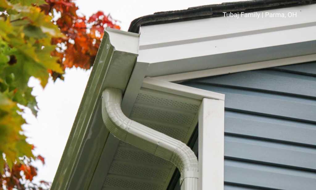 An underside view of a gutter, end cap, and elbow on the side of a blue house.