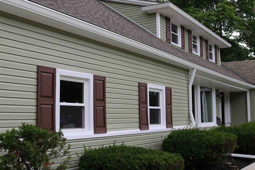 Sage green siding with maroon shutters and white double-hung windows