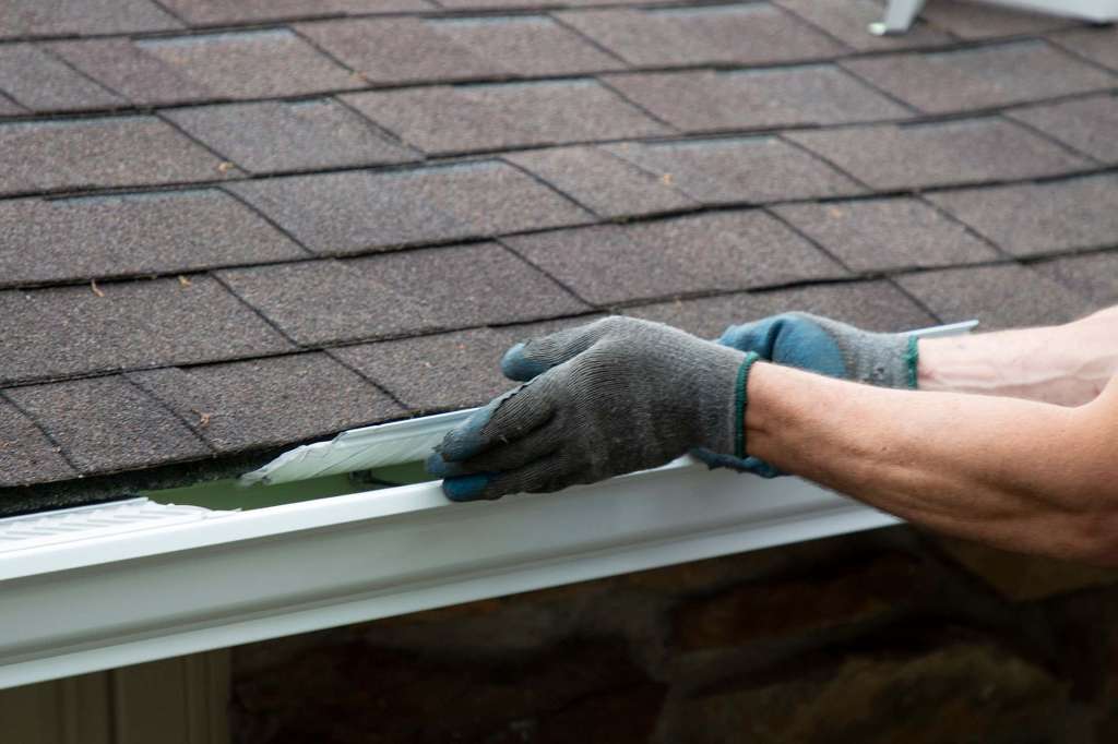 Gutter guard being fitted beneath roof shingles
