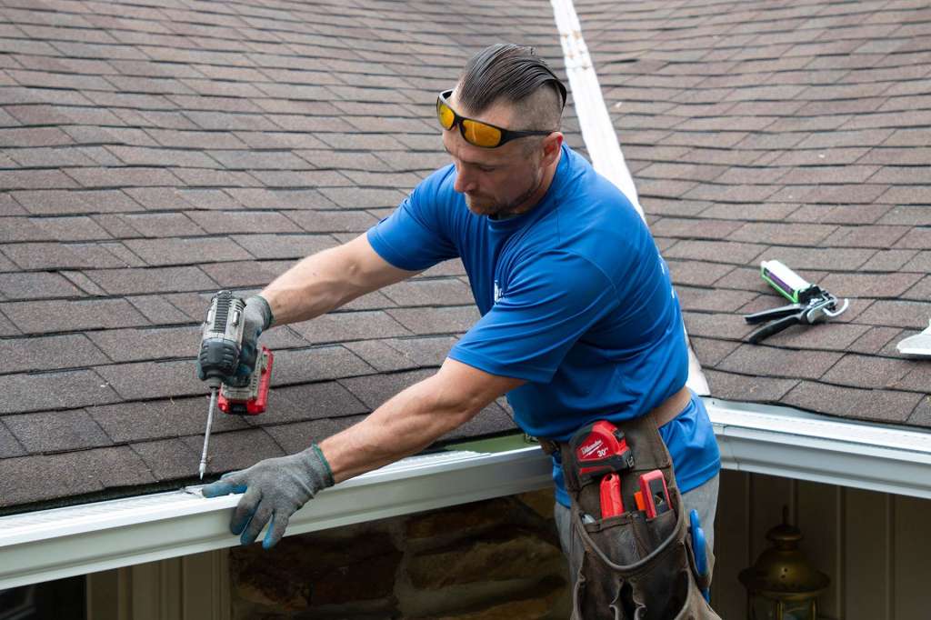 Installer fastening gutter guards at the roof edge