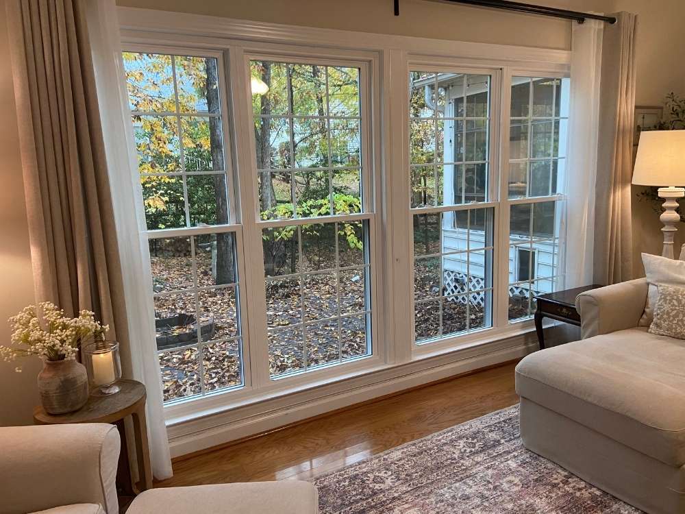 White gridded, double-hung windows create a view from the living room of a back yard covered in fall leaves. Windows installed by Universal Windows Direct .