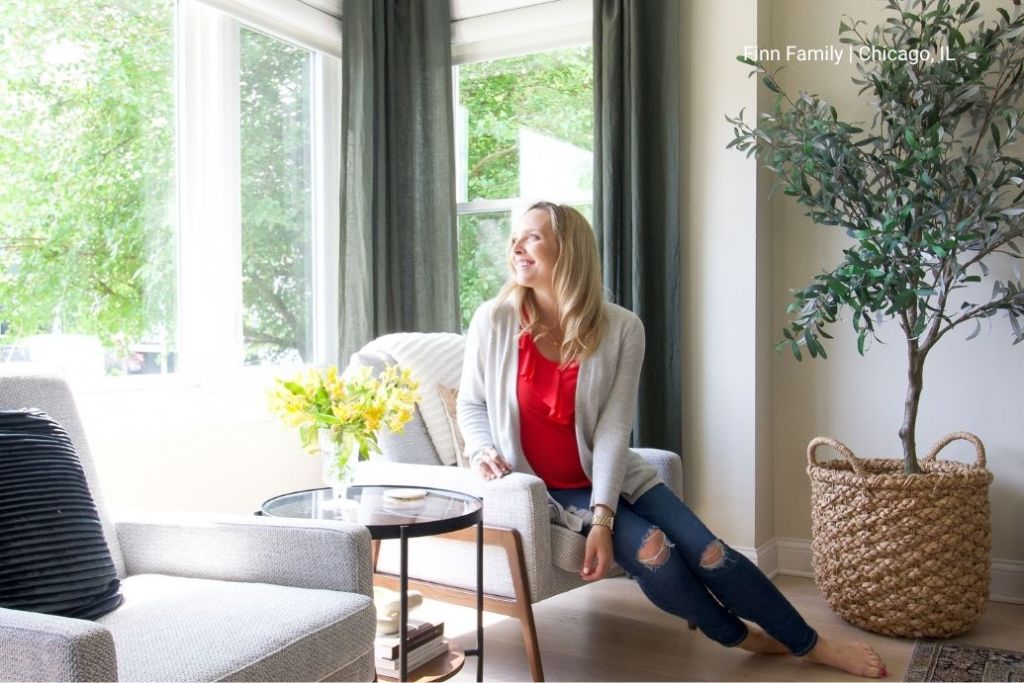 A woman smiles as she sits on her couch looking out her new windows.