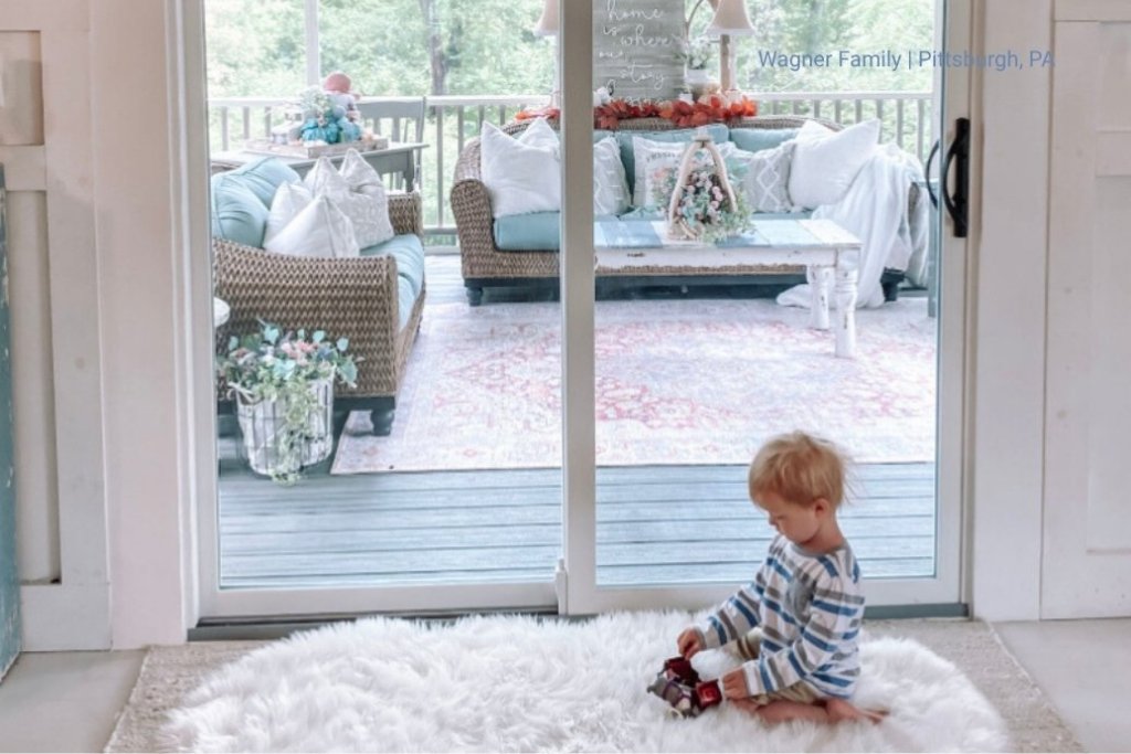 A little boy plays on a shag rug in front of a sliding patio door.