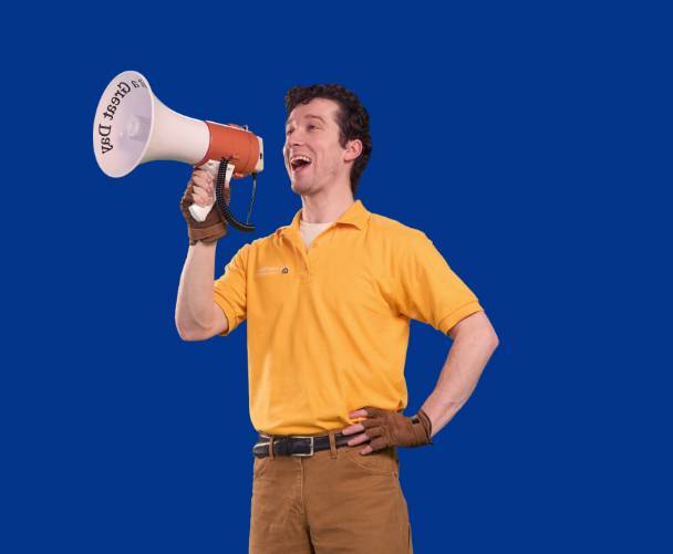 A man in a Great Day Improvements shirt stands smiling with a megaphone.