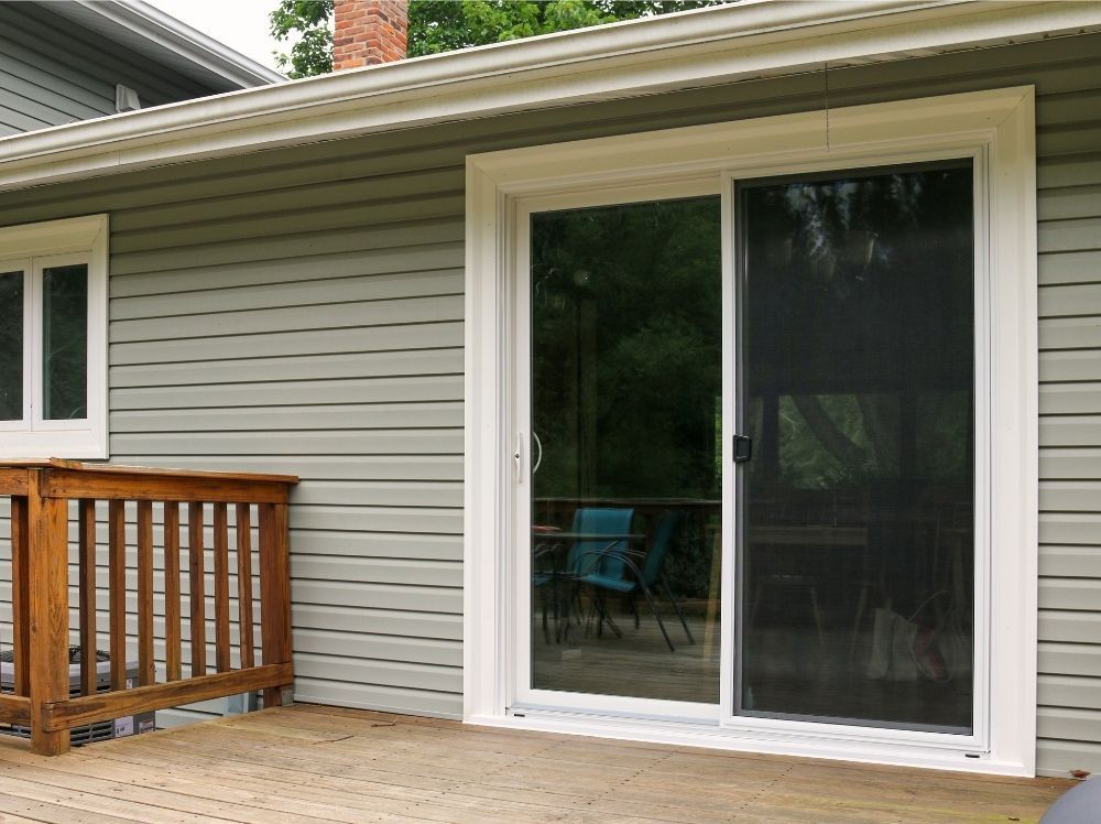A white sliding patio door with sliding screen door installed by Universal Windows Direct in front of a back deck.