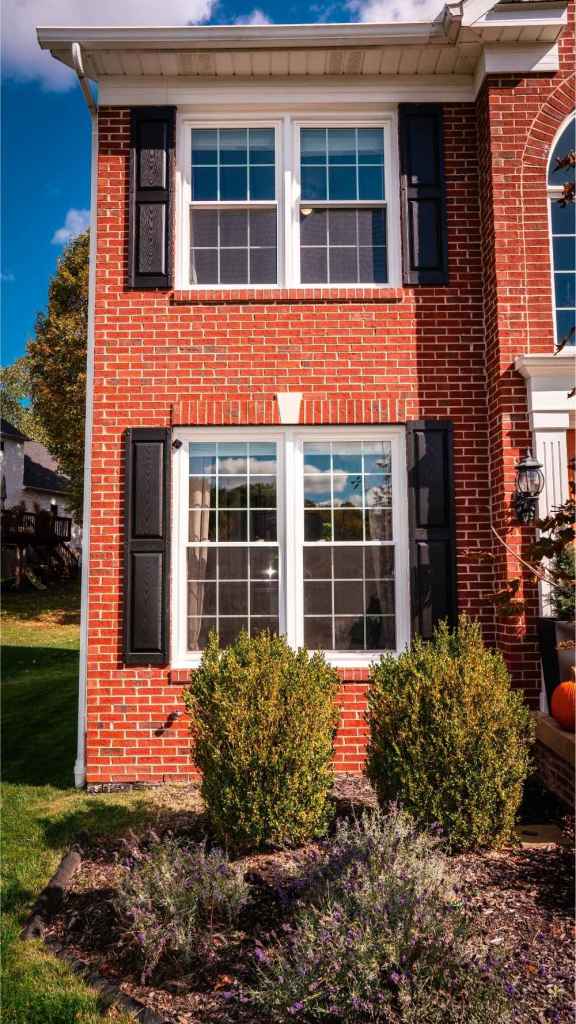 White, gridded windows with black shutters on a brick house. Windows installed by Universal Windows Direct.