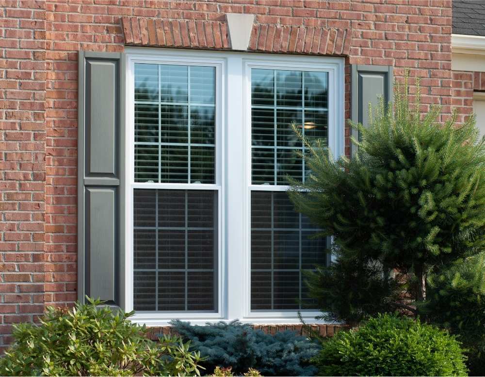 White, grided, double-hung windows with black shutters on a brick house installed by Universal Windows Direct.