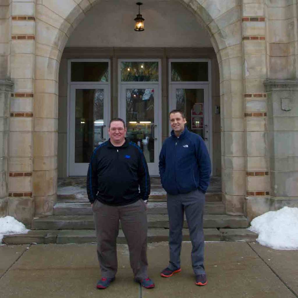 Bill Barr and Mike Strmac standing outside the entrance of Fairview High School