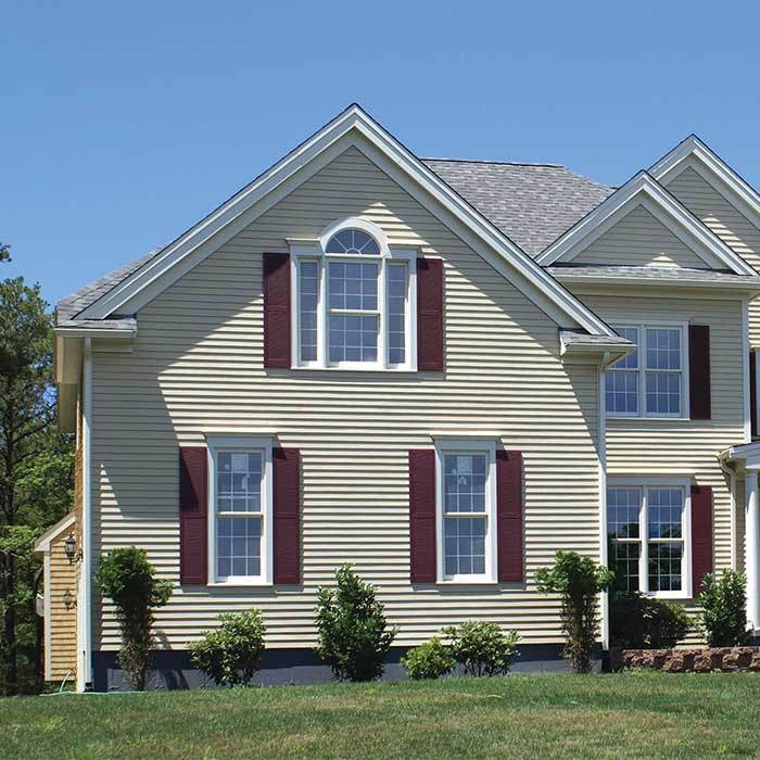 Two-story home clad in cream vinyl siding with burgundy shutters