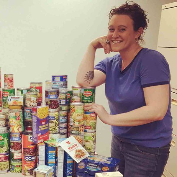 Universal Windows Direct employee beside a stack of donated canned goods