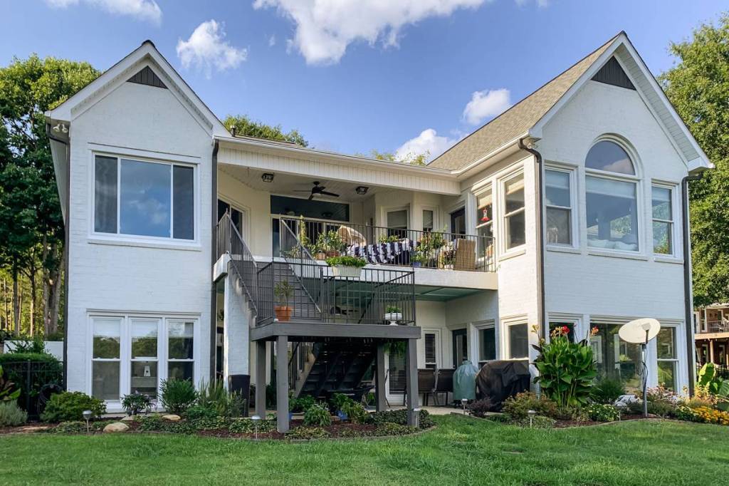 Rear of a white brick home with large picture windows overlooking the lawn