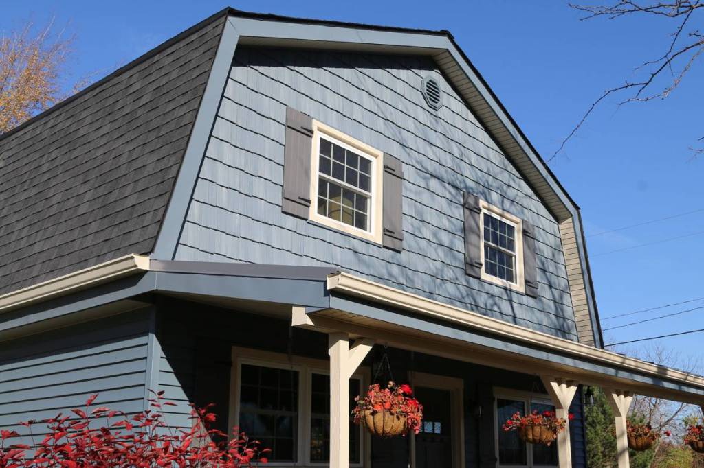 Gambrel roof gable clad in blue vinyl shakes with lap siding and a covered porch below