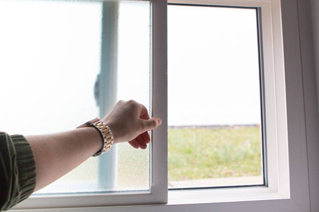 Hand sliding open a white vinyl sliding window with a view of the lawn