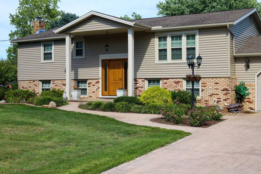 Split-level home with tan vinyl siding, brick base, and a wood front door