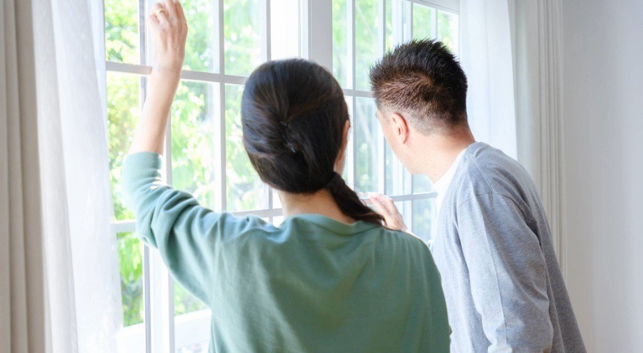 Couple looking at window from inside of the house looking out.